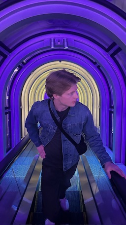 Riding an escalator through a tunnel lit in purple and yellow neon